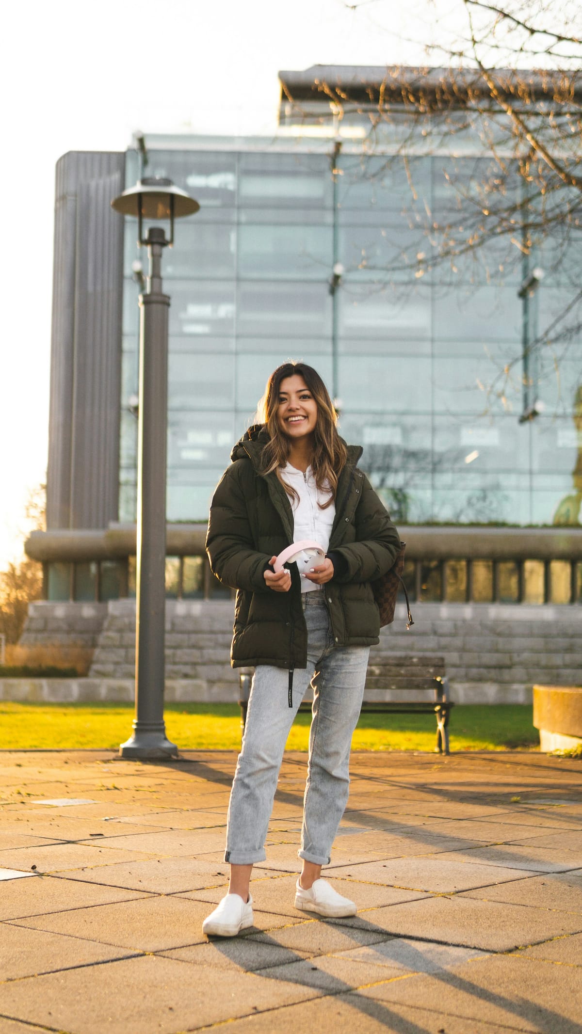A smiling student in a green puffer jacket standing on a campus plaza at golden hour