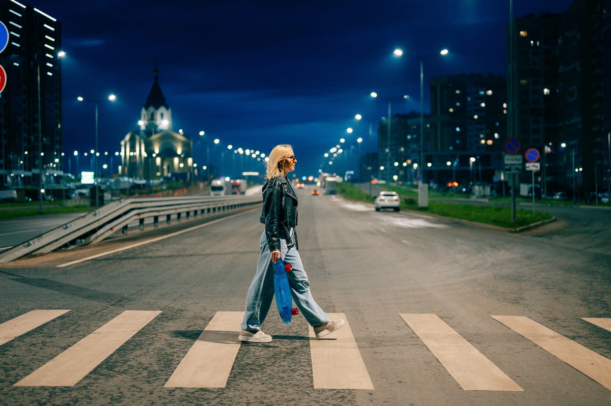 A woman crossing a city street at dusk, walking with confidence