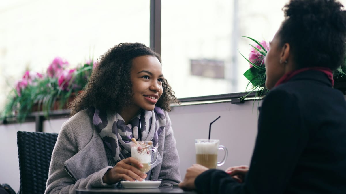 A young woman smiling across a cafe table during a conversation