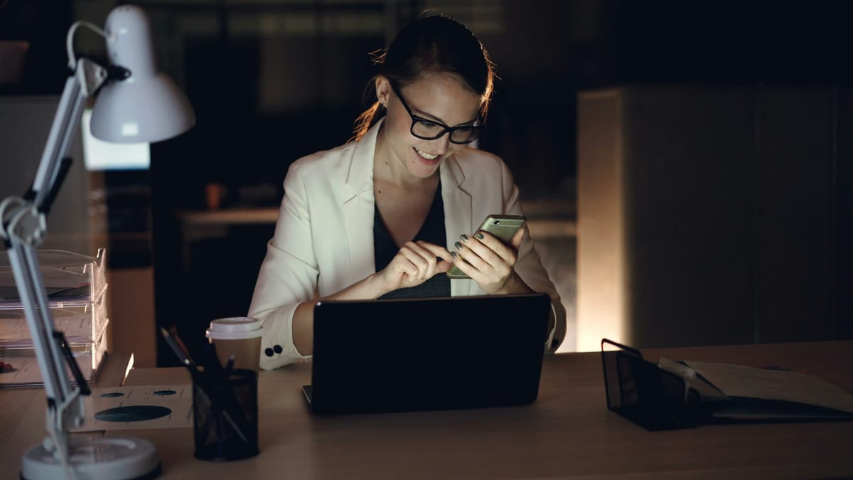A professional smiling at her phone while working late at her desk